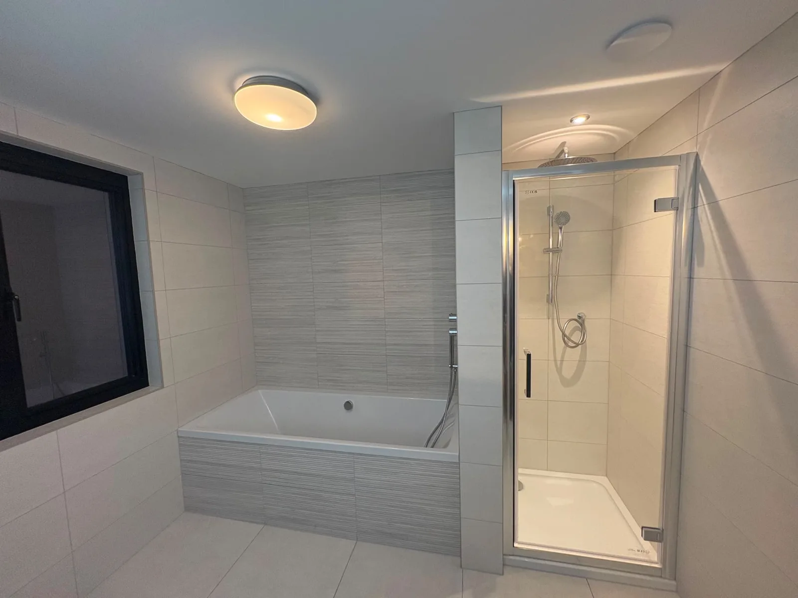 Built-in bath and tiled shower enclosure fitted in modern tiled bathroom with grey accent wall
