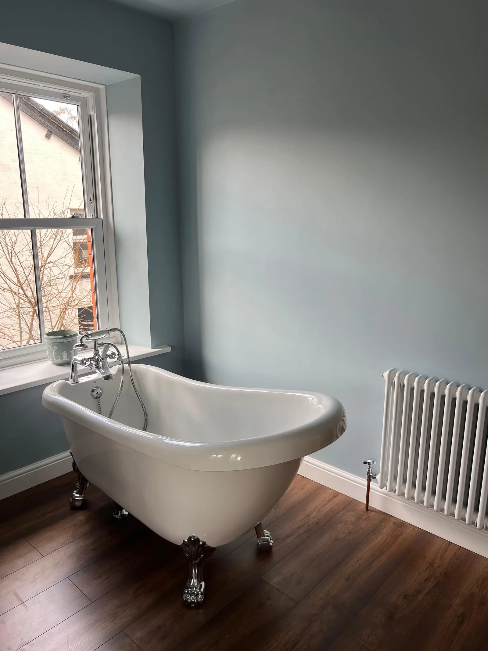 Clawfoot freestanding bath installed beside column radiator in light-blue residential bathroom